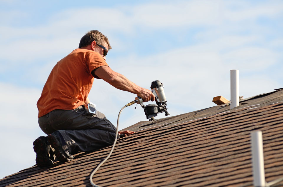 Building contractor putting the asphalt roofing on a large commercial apartment building