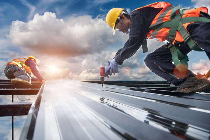 Worker builder with hand drill at metal profile roof installation Metal roof construction