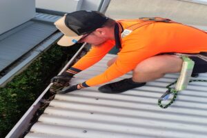 Roof worker wearing safety gear while cleaning gutters